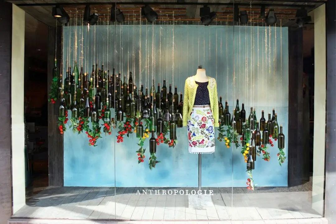 Cửa sổ trưng bày nghệ thuật với vật dụng treo từ trần và mannequin giữa backdrop xanh pastel.